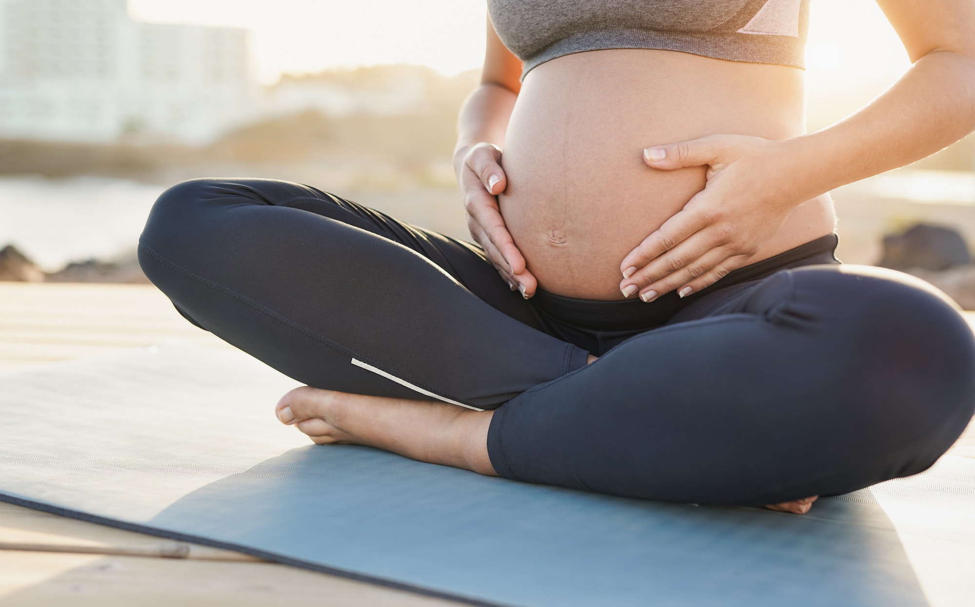 Pregnant woman touching her belly after yoga exercise outdoor at sunrise